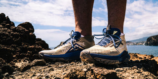 Image of a man's feet wearing Nike Trail running shoes while stood on a rocky coastal surface